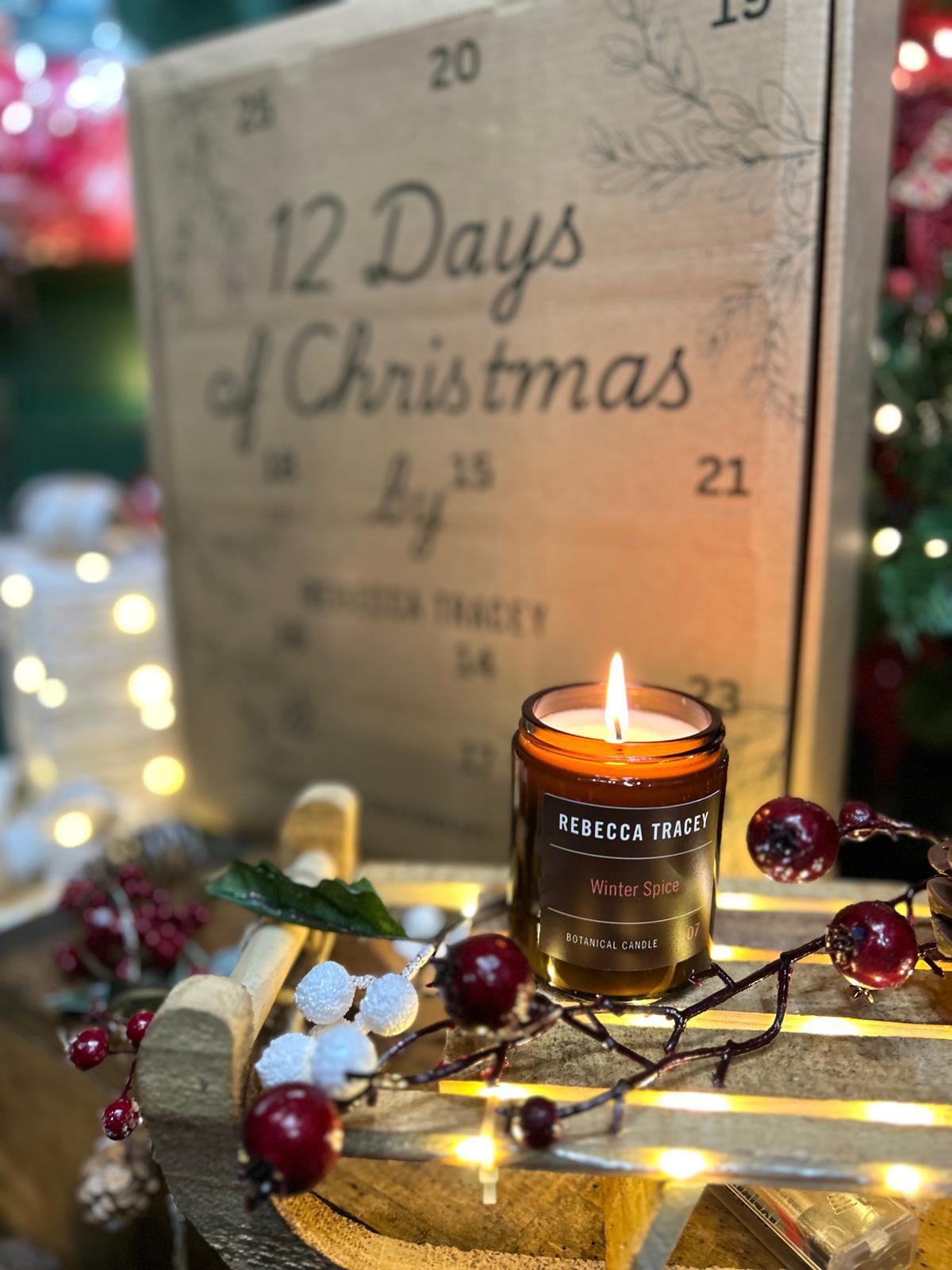 Candle with a wooden '12 Days of Christmas' advent calendar in the background