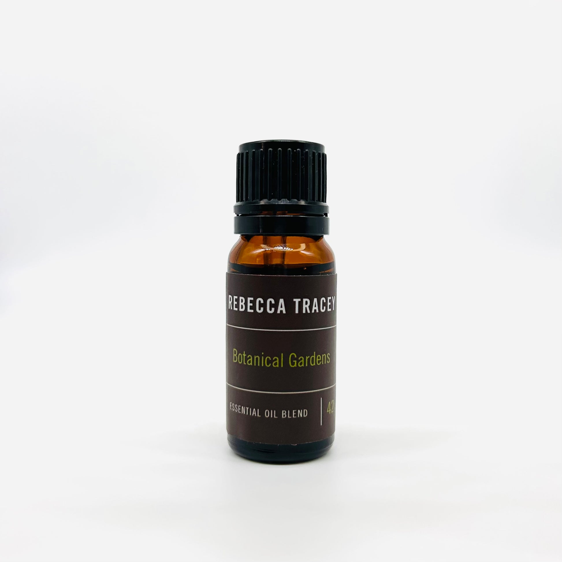 A small amber glass bottle of Rebecca Tracey Botanical Gardens essential oil blend with a black cap and dark brown label, centered on a white background.