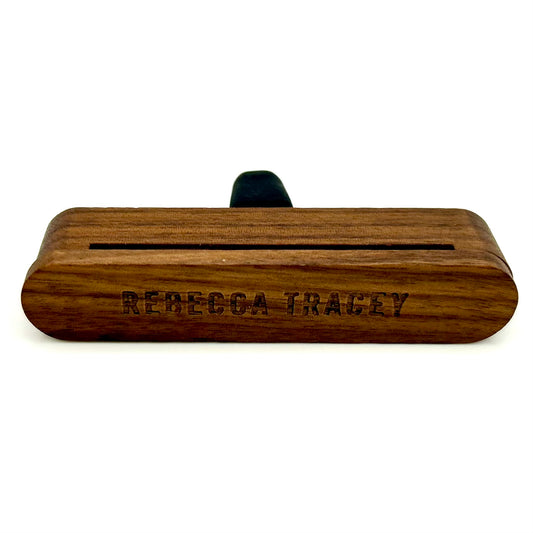 A personalized wooden keepsake box with rounded corners, featuring the engraved name 'REBECCA TRACEY' on the front and a small black ribbon loop on top, set against a plain white background.