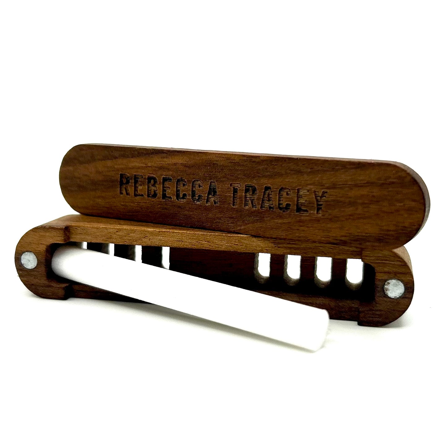 A wooden smoking accessory holder with a white rolled joint or pipe resting inside, photographed on a clean white background. The wooden lid is engraved with the name 'REBECCA TRACY'.