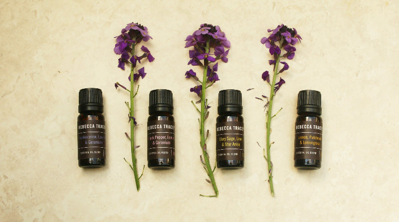 Five bottles of Rebecca Tracey essential oils with purple flowers on a textured beige background