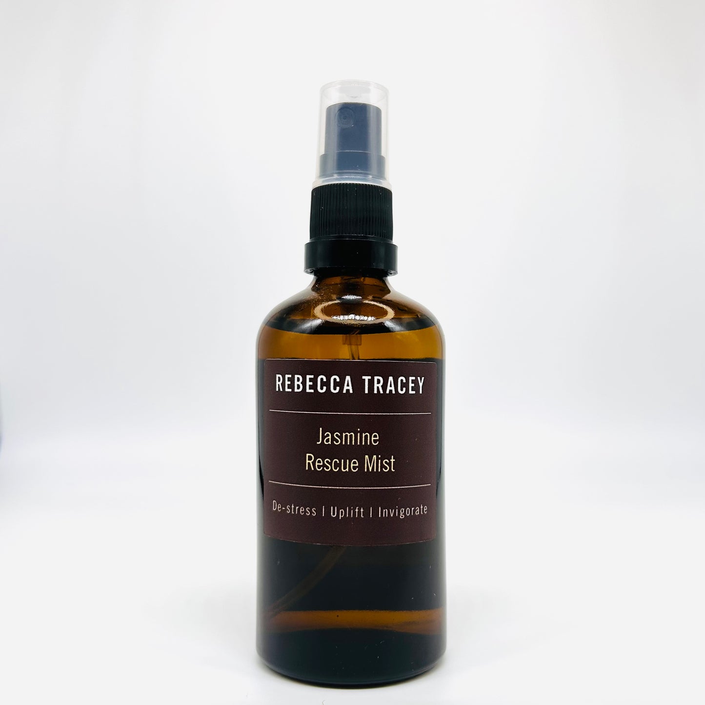 An amber glass spray bottle of Rebecca Tracey Jasmine Rescue Mist with a black spray nozzle and a dark brown label, set against a plain white background.
