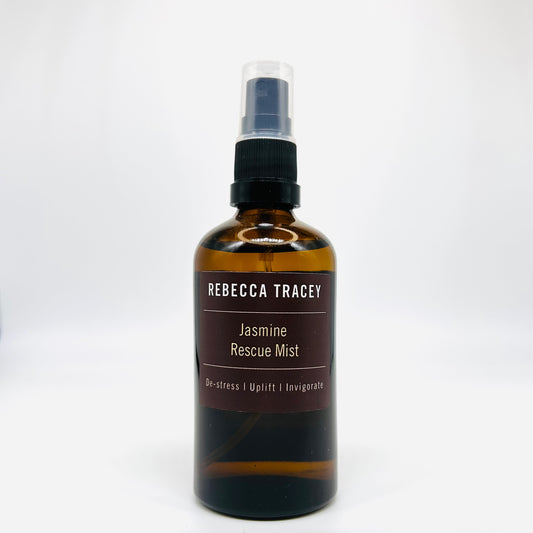 An amber glass spray bottle of Rebecca Tracey Jasmine Rescue Mist with a black spray nozzle and a dark brown label, set against a plain white background.