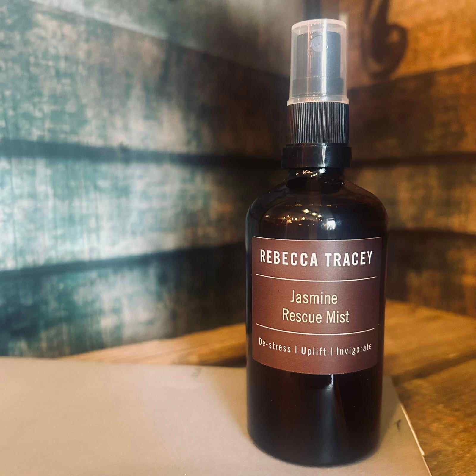 Bottle of Rebecca Tracey Jasmine Rescue Mist on a wooden surface with a blurred background