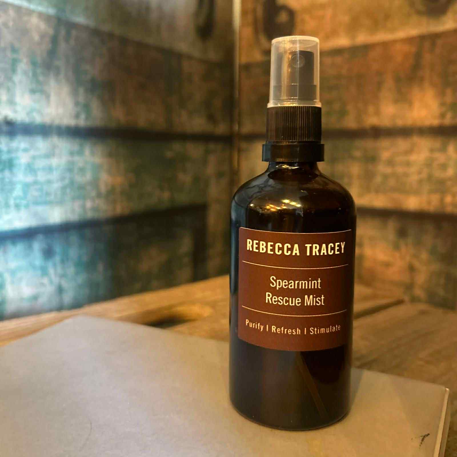 Bottle of Rebecca Tracey Spearmint Rescue Mist on a wooden surface with a patterned wall in the background.