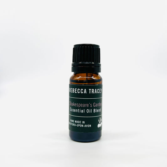 A small amber glass bottle of Rebecca Tracey 'Shakespeare's Garden' essential oil blend with a black cap and a dark green label, set against a plain white background.