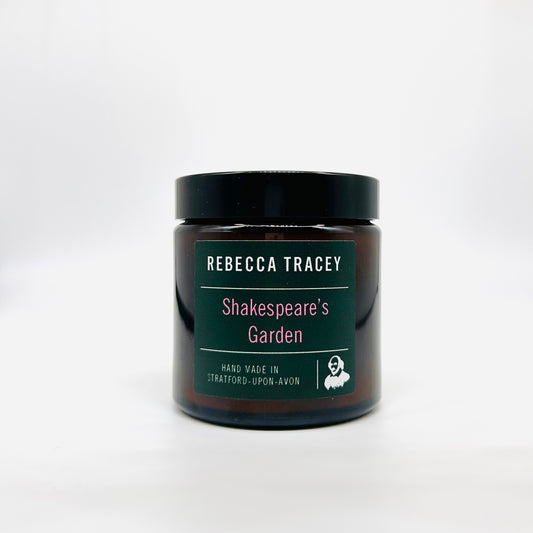 A dark amber glass jar with a black lid and a dark green label reading 'REBECCA TRACEY Shakespeare's Garden' on a light gray background.