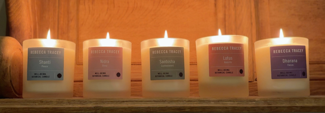 Five lit candles with labels on a wooden shelf.
